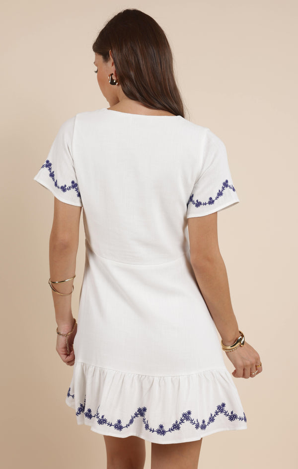 back view of the model wearing the timeless mini dress. shows the flutter sleeves. also shows the embroidered detailing, the bottom ruffle and the mini length. 