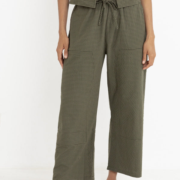 front view of the model wearing the louise check pants. shows the drawstring waistband. also shows the front patch pockets, the high rise and the olive checkered print. 