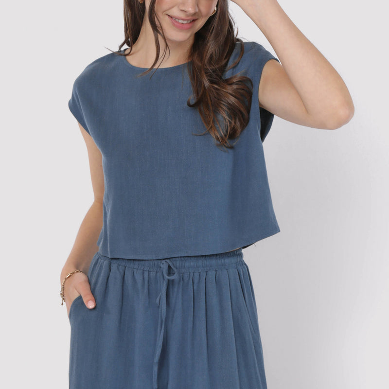 front view of the model wearing the sugarloaf linen top. shows the crew neckline. also shows the cap sleeves, the blue color and the waist length. 