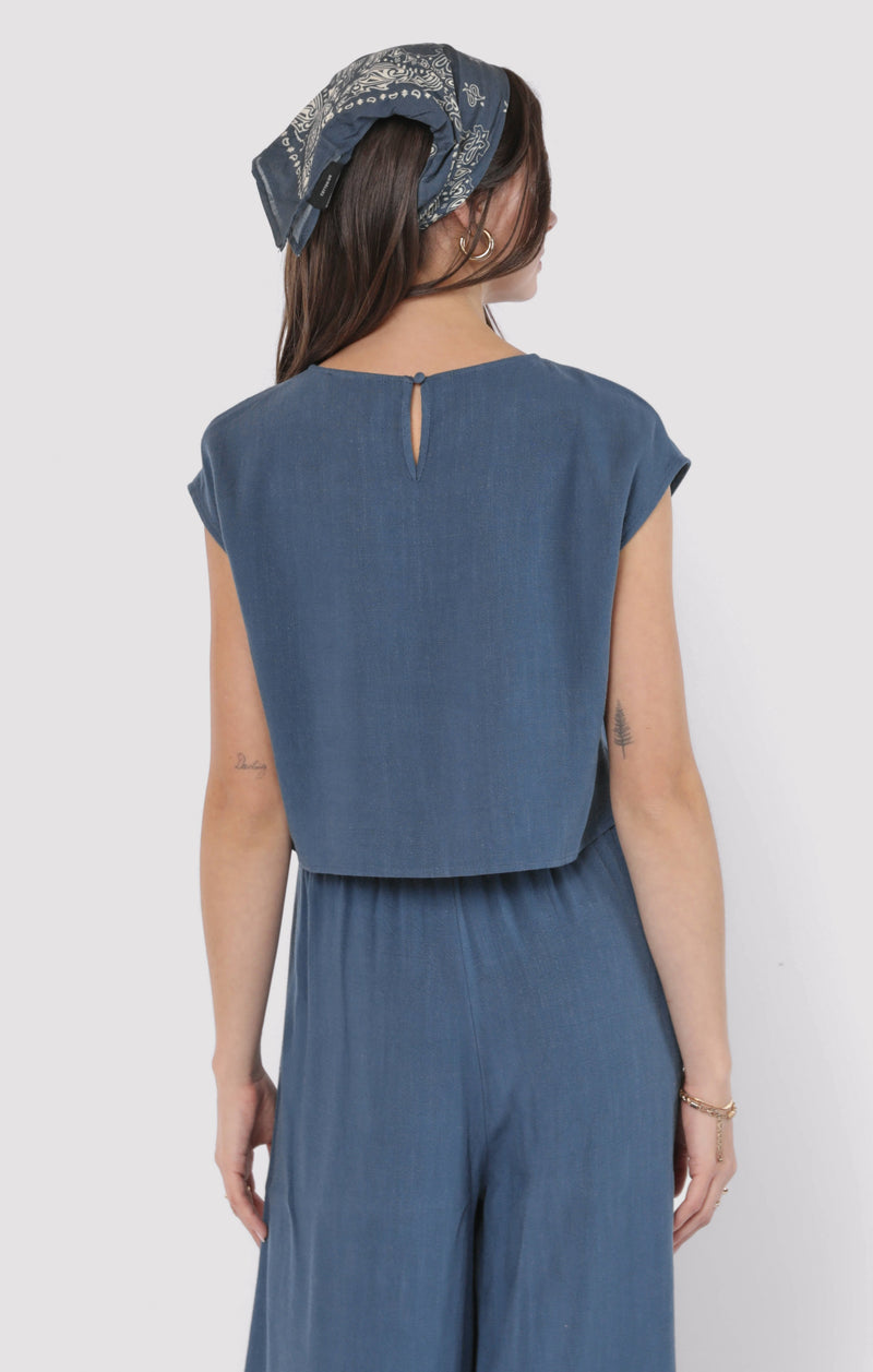 back view of the model wearing the sugarloaf linen top. shows the back keyhole. also shows the cap sleeves, the blue color and the waist length 