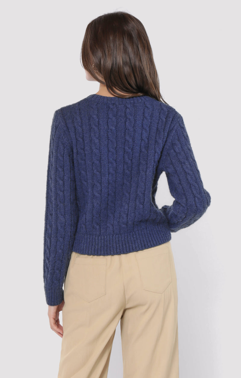 back view of the model wearing the lulu embroidered daisy sweater. shows the cable knit detail. also shows the navy color, and the waist length. 
