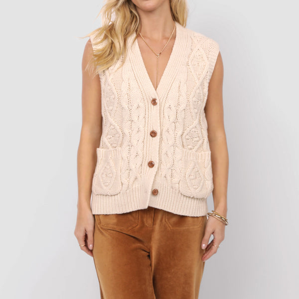Woman wearing a cream knitted vest over a brown top with a white background
