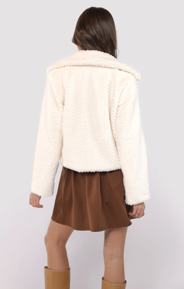 Person wearing a white sherpa jacket and brown skirt on a plain background
