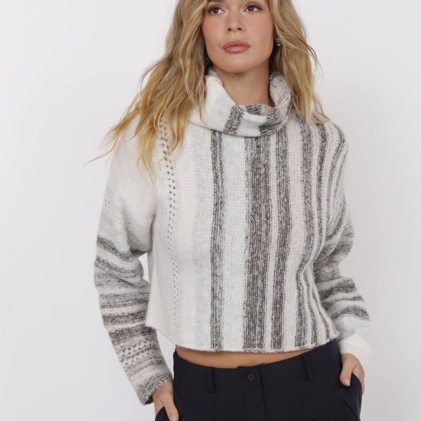 Woman wearing a white and gray striped sweater with black pants on a white background