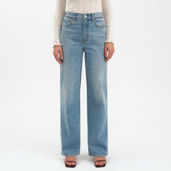 Person wearing a white long-sleeve top and light blue jeans on a white background