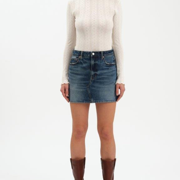 Person wearing a white sweater, blue denim skirt, and brown boots on a white background