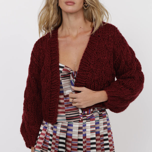 Woman wearing a burgundy cardigan over a colorful striped dress on a white background