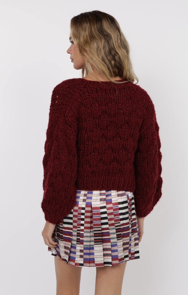 Woman wearing a burgundy cable knit sweater and patterned skirt on a white background