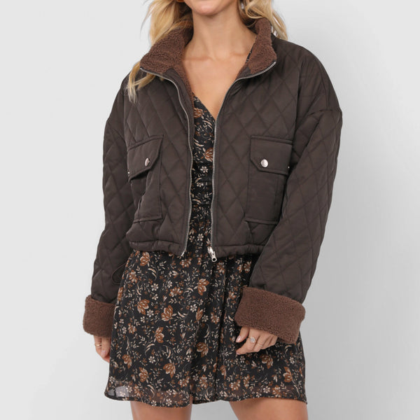 Woman wearing a brown quilted jacket over a floral dress on a white background