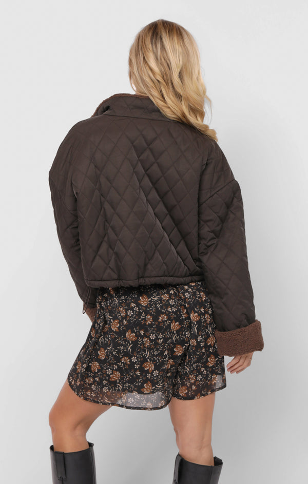 Person wearing a brown quilted jacket and floral skirt on a white background