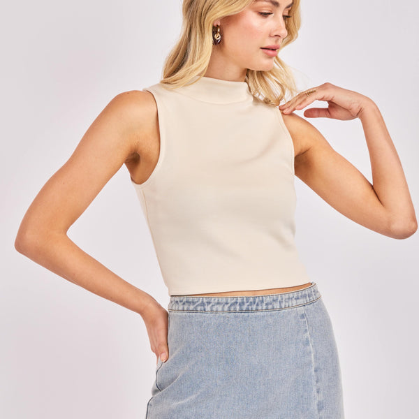 Woman wearing a beige sleeveless top and denim skirt on a plain background