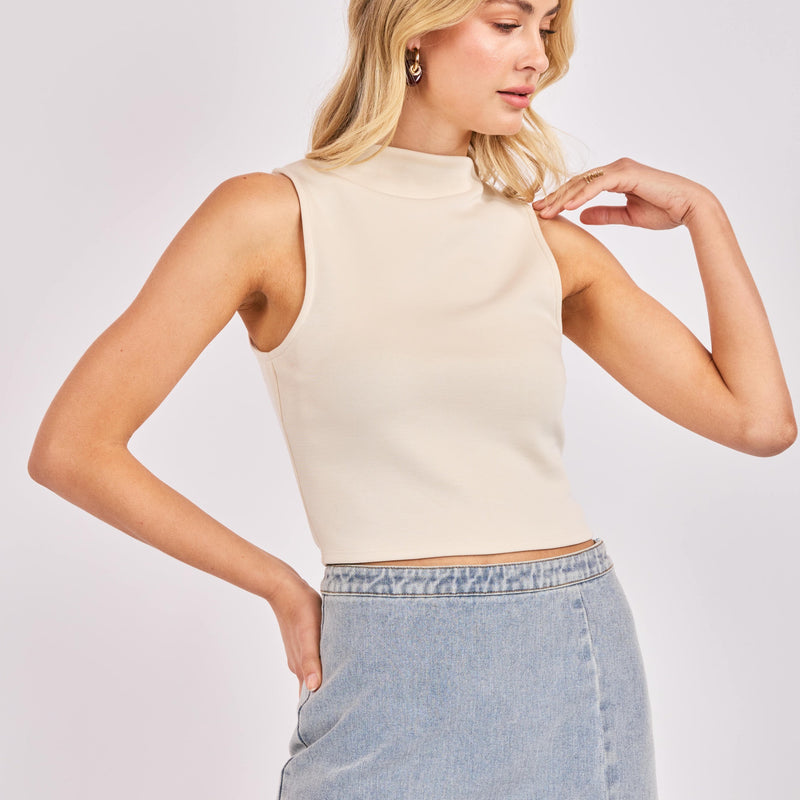 Woman wearing a beige sleeveless top and denim skirt on a plain background