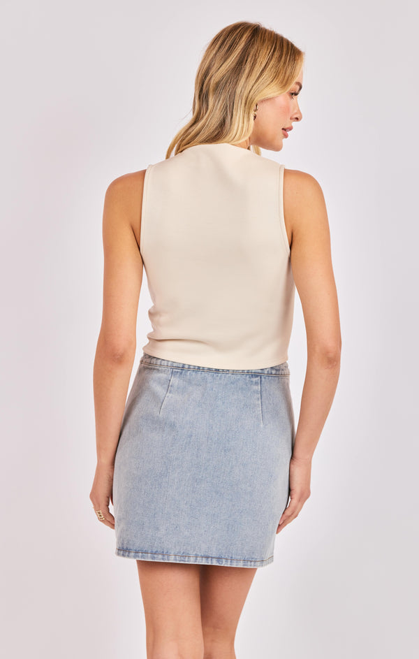 Woman wearing a beige sleeveless top and light blue denim skirt on a white background