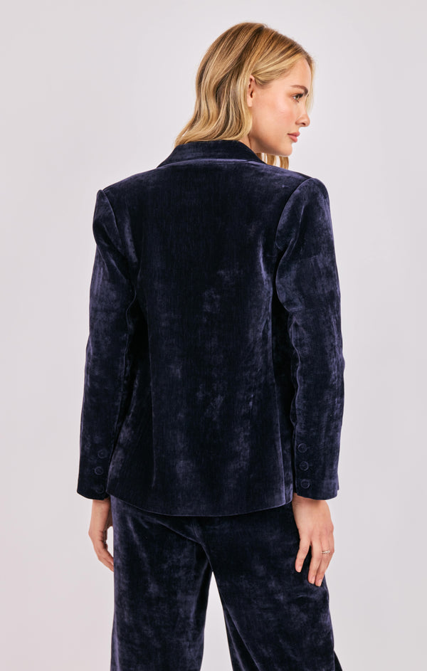 Woman wearing a navy velvet blazer and pants on a light gray background