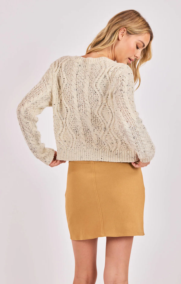 Woman wearing a beige cable knit sweater and mustard yellow skirt on a white background