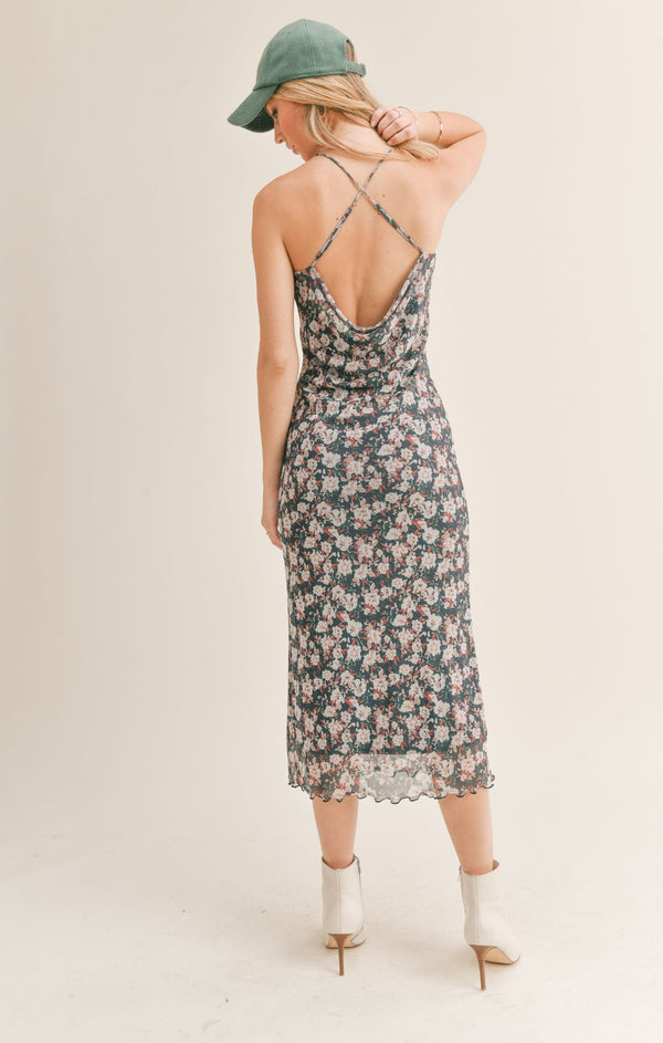 Back view of model wearing midi dress. Shows the back criss cross straps. Also shows the back cowl and the lettuce style hem. 