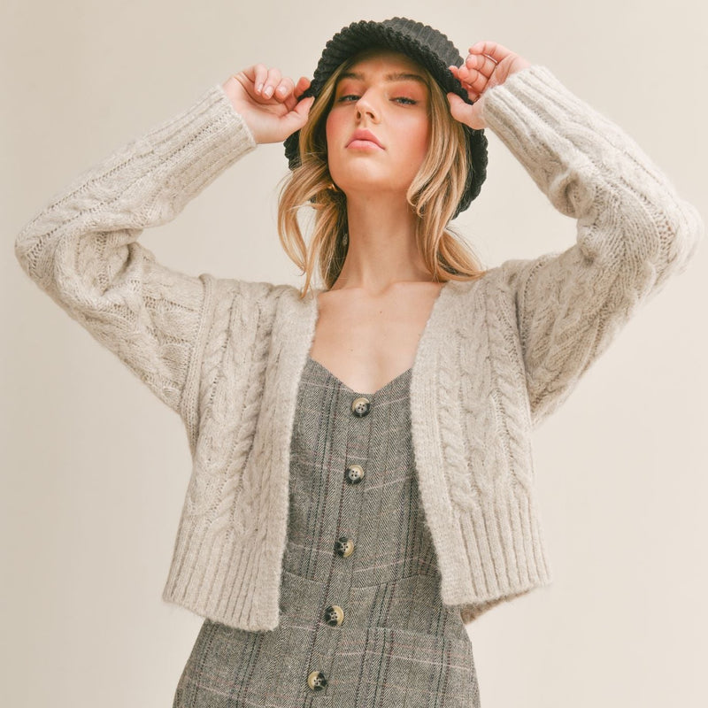 Front view of model wearing cardigan. Shows the open front. Also shows the cable knit detail and that the sweater is cropped. 