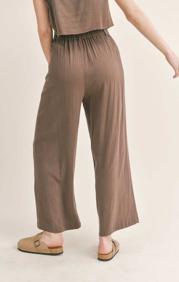 Back view of the model wearing the linen pants. Shows the synched back and the belt loops. Also shows that they are an ankle length. 