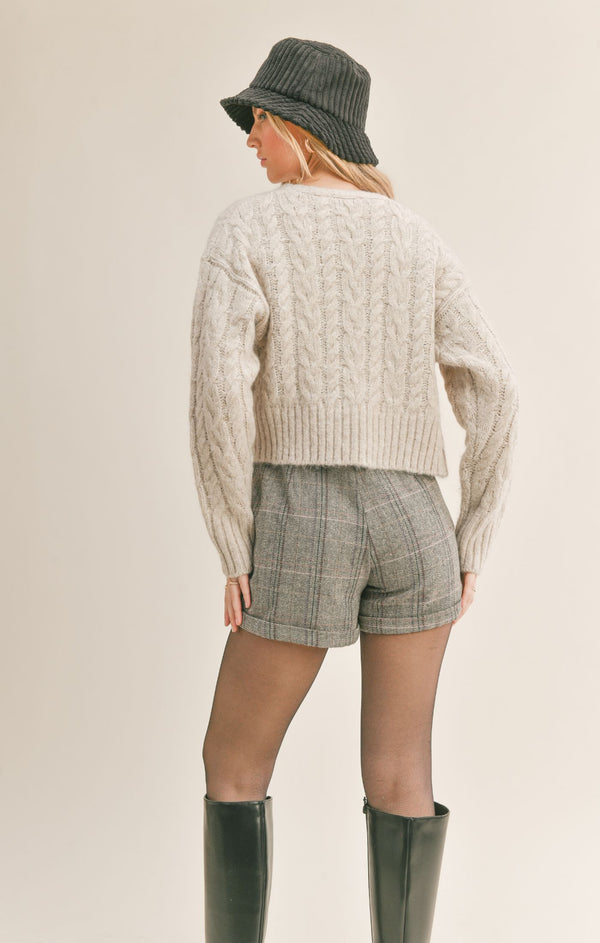 Back view of model wearing cardigan. Shows the dropped shoulder seams. Also shows the cable knit detailing and that sweater is a crop length.