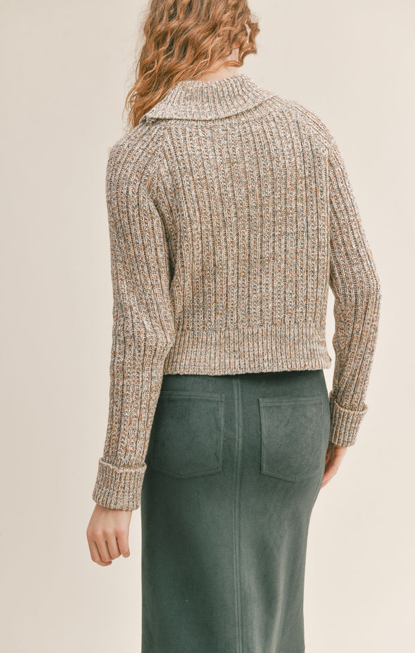 Back view of model wearing sweater. Shows the ribbed folded cuffs. Also shows the back side of the turtleneck and ribbed hem. 