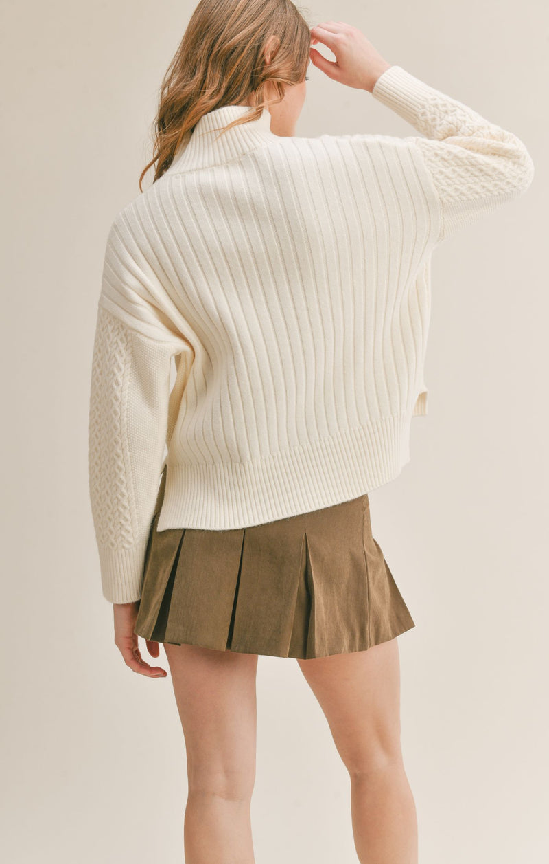 Back view of the model wearing the sweater. Shows some of the side slits. Also shows that the back is longer and the long sleeves.