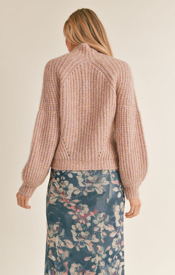 back view of model wearing the Malory sweater in pink. shows the mock neck. also shows the slight puff sleeves, the knit detail and the ribbed cuffs and hems.