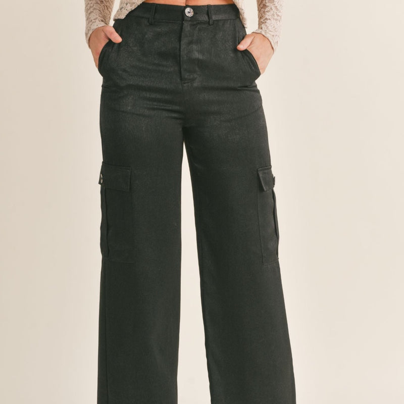 front view of model wearing Aphrodite cargo pants in black. shows the button closure. also shows the top and side cargo pockets, the belt loops and a slight shine to the pants.