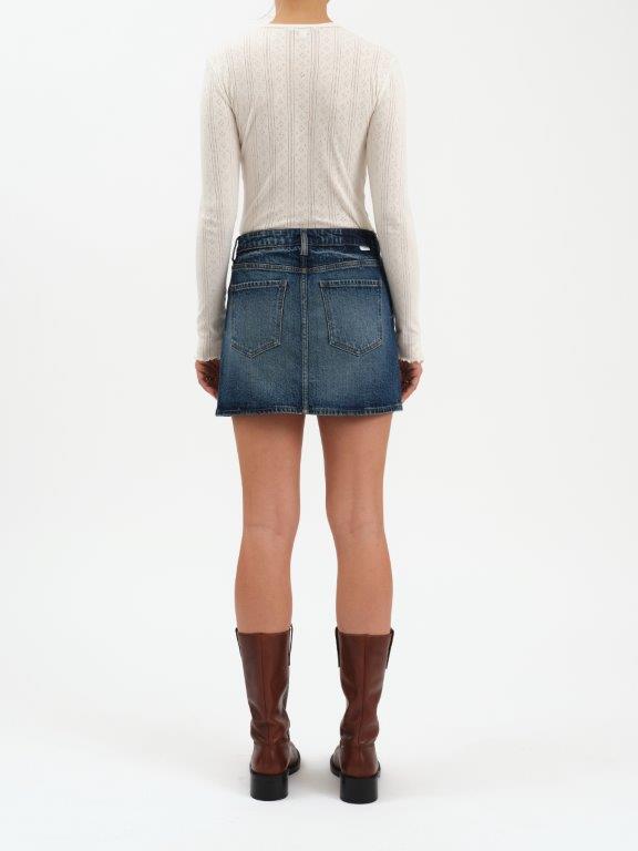 Person wearing a white sweater, blue denim skirt, and brown boots on a white background