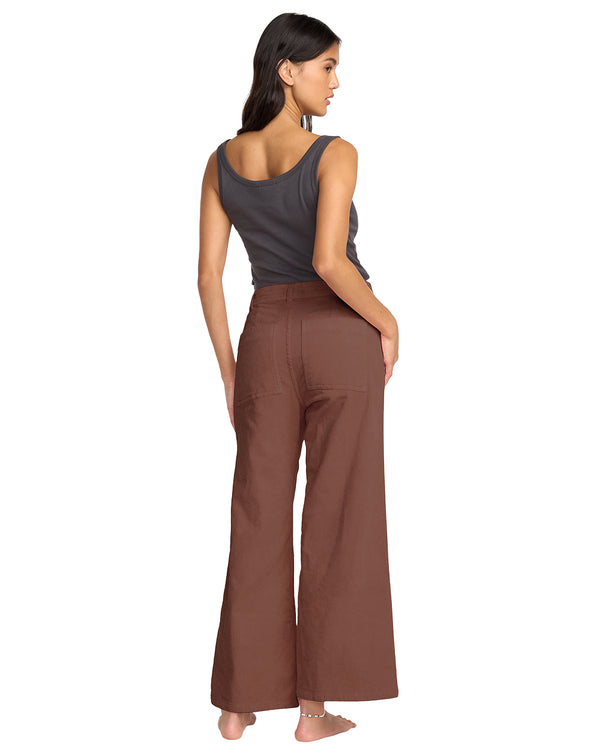Woman wearing a gray tank top and brown wide-leg pants on a white background