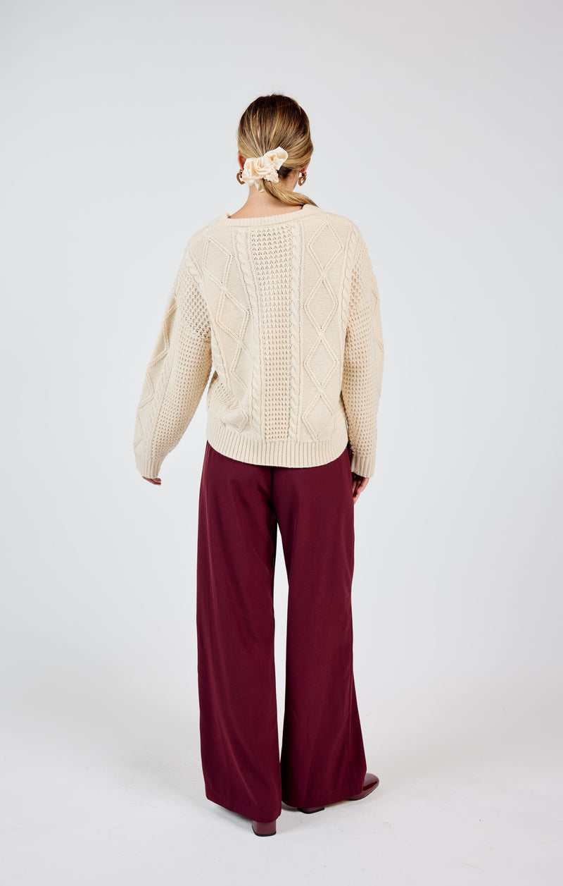 back view of the model wearing the teri cable crewneck sweater. shows that the back is alittle longer than the front. also shows the cable knit detailing and the ribbed detailing and the crew neckline.  