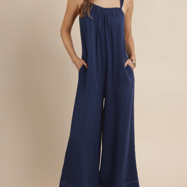 front view of the model wearing the breezy lane jumpsuit. shows the square neckline. also shows the straps, the side pockets, the wide legs and the white stitching. 