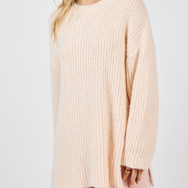 front view of the model wearing the your needs sweater in this cream color. shows the dropped shoulders. also shows the crew neckline, the side slots and the ribbed detailing. 