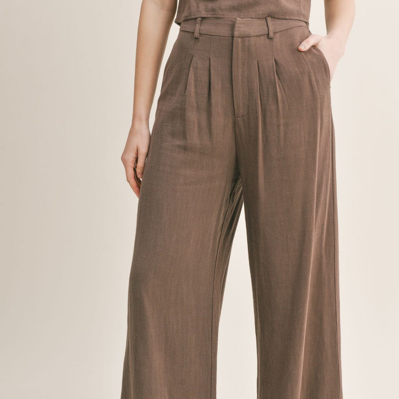 Front view of the model wearing the linen pants. Shows the pleating and the belt loops. Also shows that they are high waisted. 