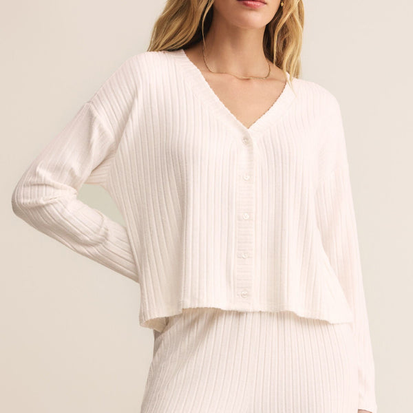 Woman wearing a white ribbed blouse and pants against a light background