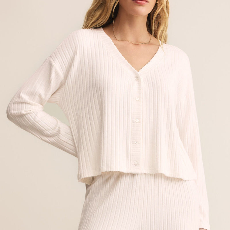 Woman wearing a white ribbed blouse and pants against a light background
