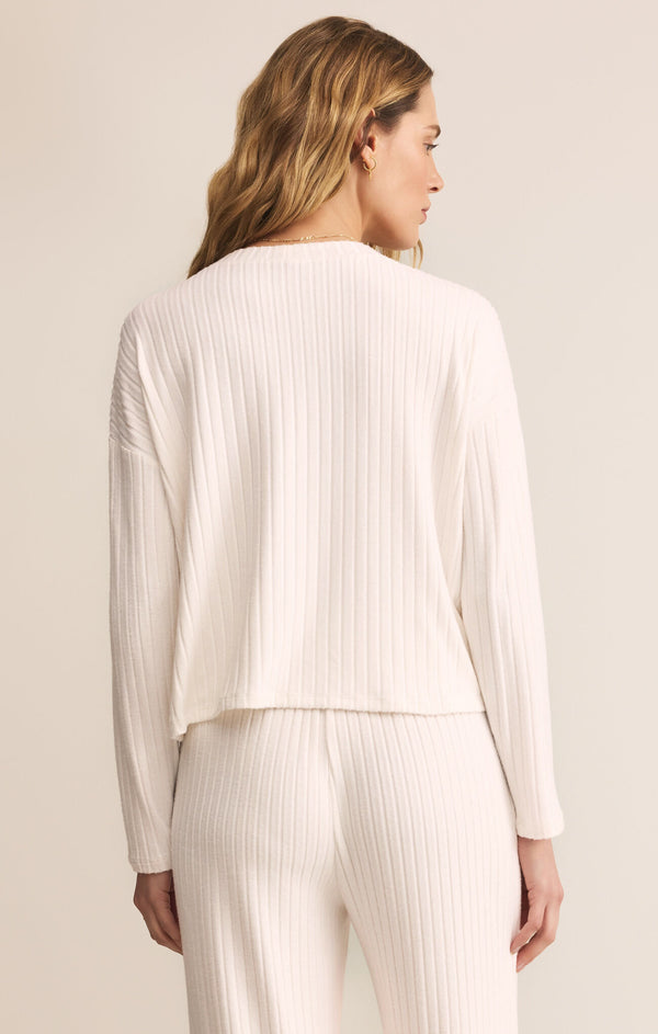 Woman wearing a white ribbed long-sleeve top and pants against a beige background