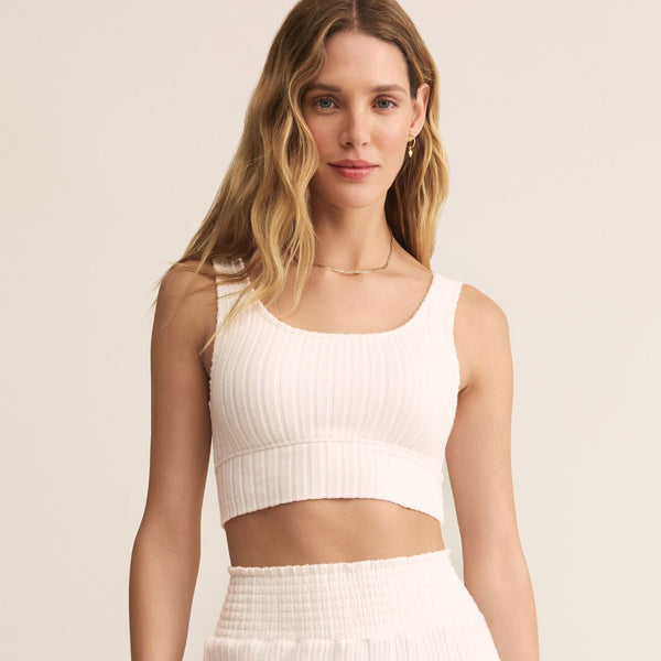Woman wearing a white ribbed crop top and high-waisted pants against a beige background