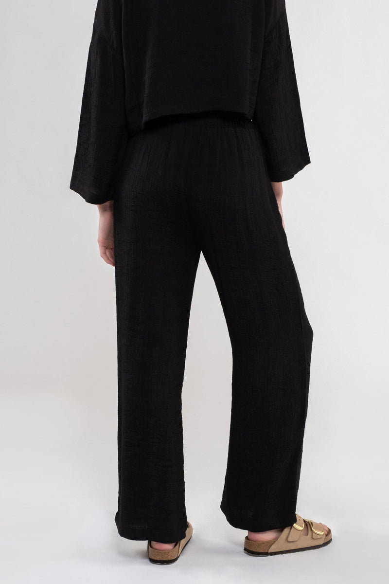 back view of the model wearing the Vivian lightweight high rise pant in black. shows the high rise of the pant. also shows that the pants are a wide leg. 