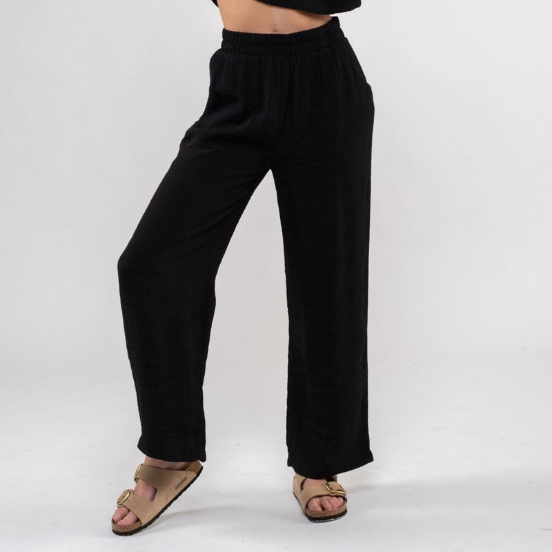 front view of the model wearing the Vivian lightweight high-rise pant in black. Shows the high rise of the pant. also shows the wide leg, the elastic waistband and the front pockets.