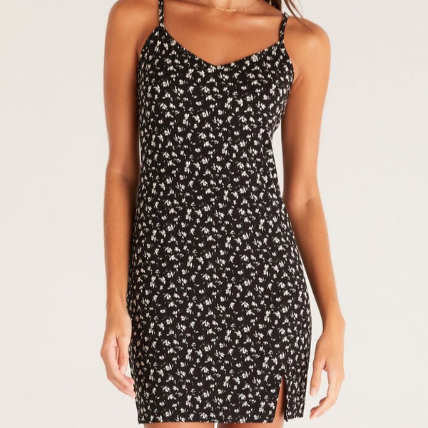 Front view of mini dress. Shows v-neckline, spaghetti straps, ditsy floral print on top of black background and small side slit.