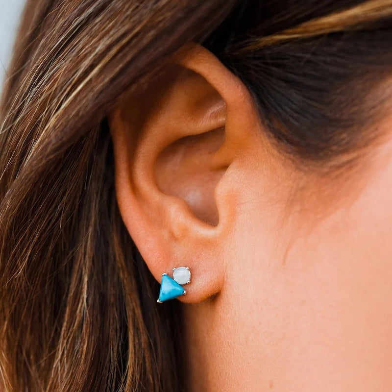 model is shown wearing earring. it features a turquoise stone in the shape of a triangle with a moonstone sitting on top 