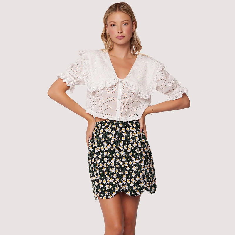 front view of model in skirt. shows a high wast, all over floral print, buttons down the front and a scalloped hemline.