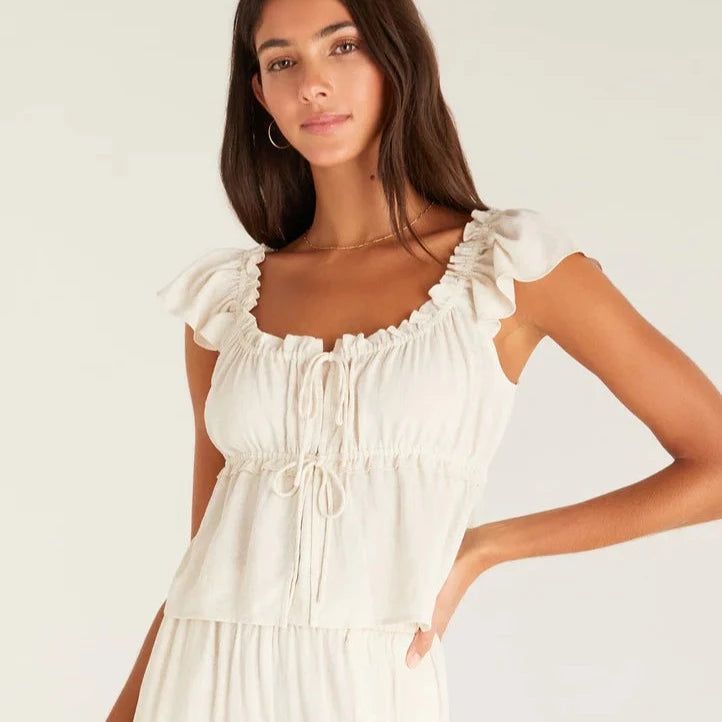 shows front view of cream blouse featuring flutter sleeves, lettuce neckline, empire tier with lettuce detail. adjustable double front tie closure and cropped silhouette.