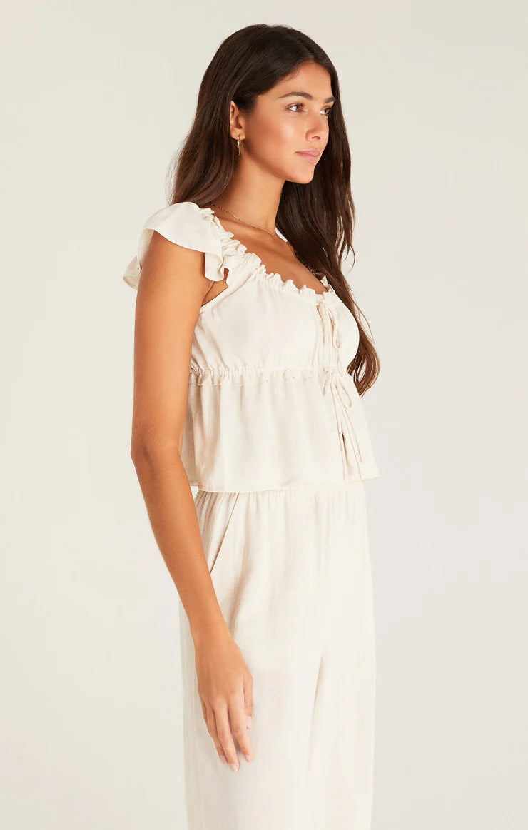 shows angled view of cream blouse featuring flutter sleeves, lettuce neckline, empire tier with lettuce detail. adjustable double front tie closure and cropped silhouette.