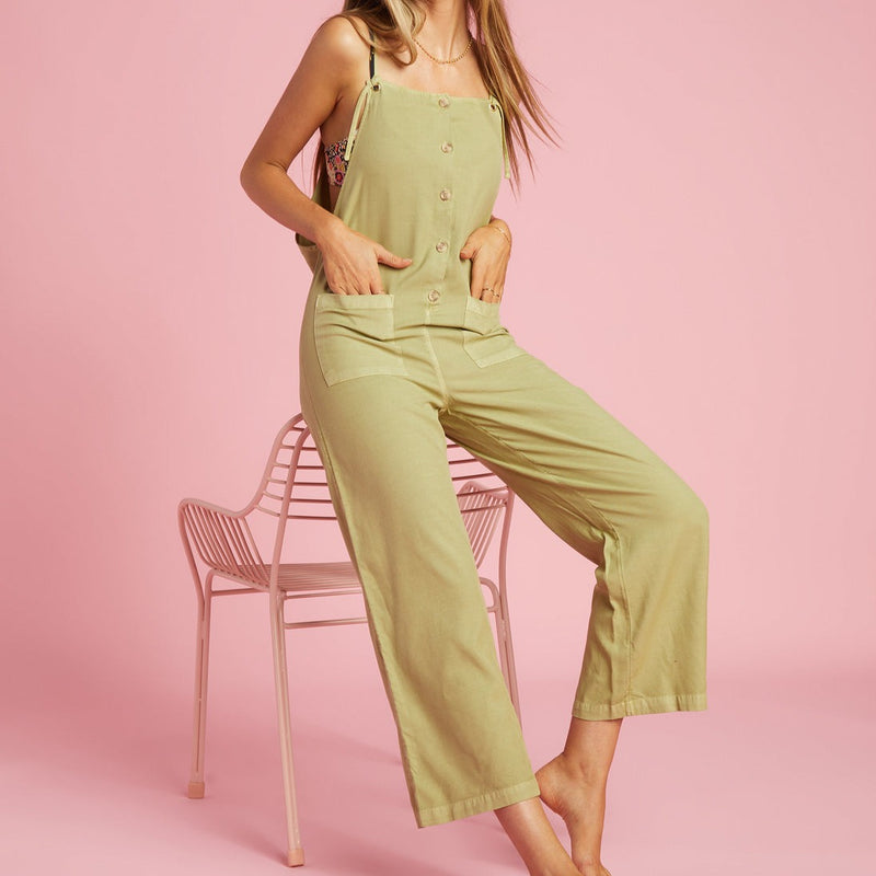 shows front view of model sitting in overalls. featuring a button up bodice, patch pockets, and adjustable tie straps. falls to the ankle 