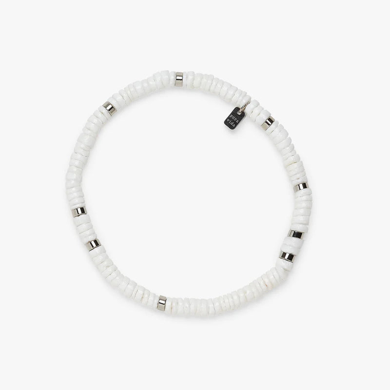 shows a white backdrop under a stretch bracelet featuring white and silver flat beads and a charm etched with "pura vida"