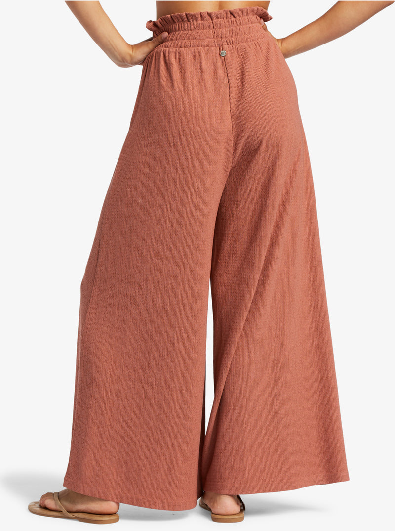 back view of model in the cedar wood pants. shows the smocked elastic waistband and the wide legs. length hits the mode at the ankle.
