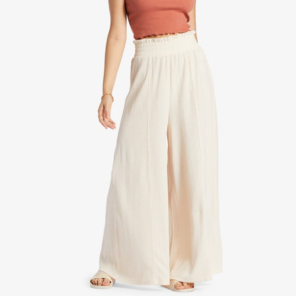 front view of model wearing the ivory (tapioca)  pants. shows the smocked, high waisted elastic waistband and wide legs.