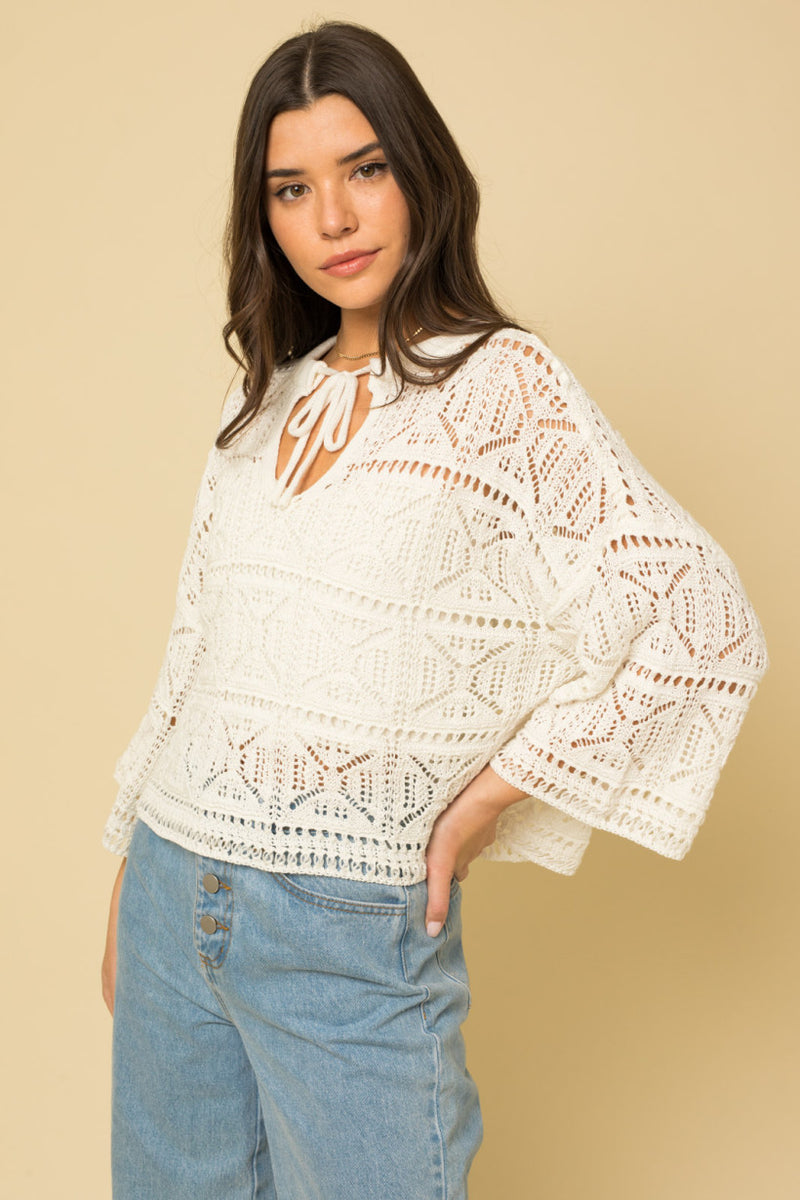 shows angled view of 3/4 sleeve crochet knit top with neck tie and a keyhole. bell sleeves with oversized fit.